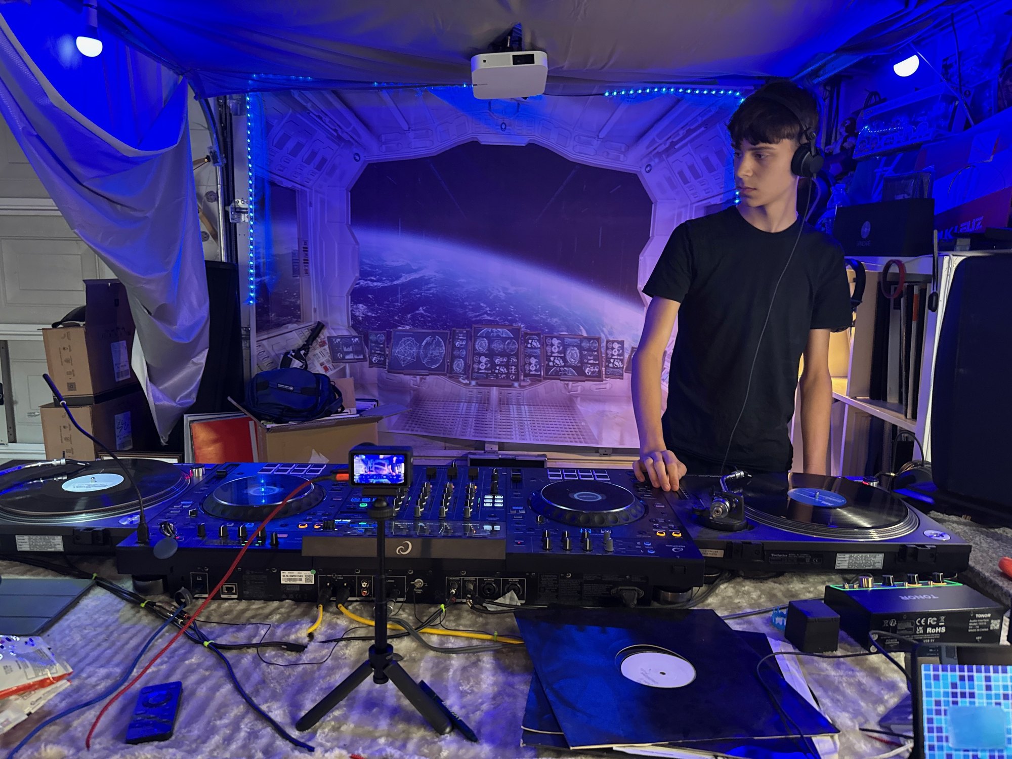 The full booth: turntables either side of the deck setup, headphones on, records out.