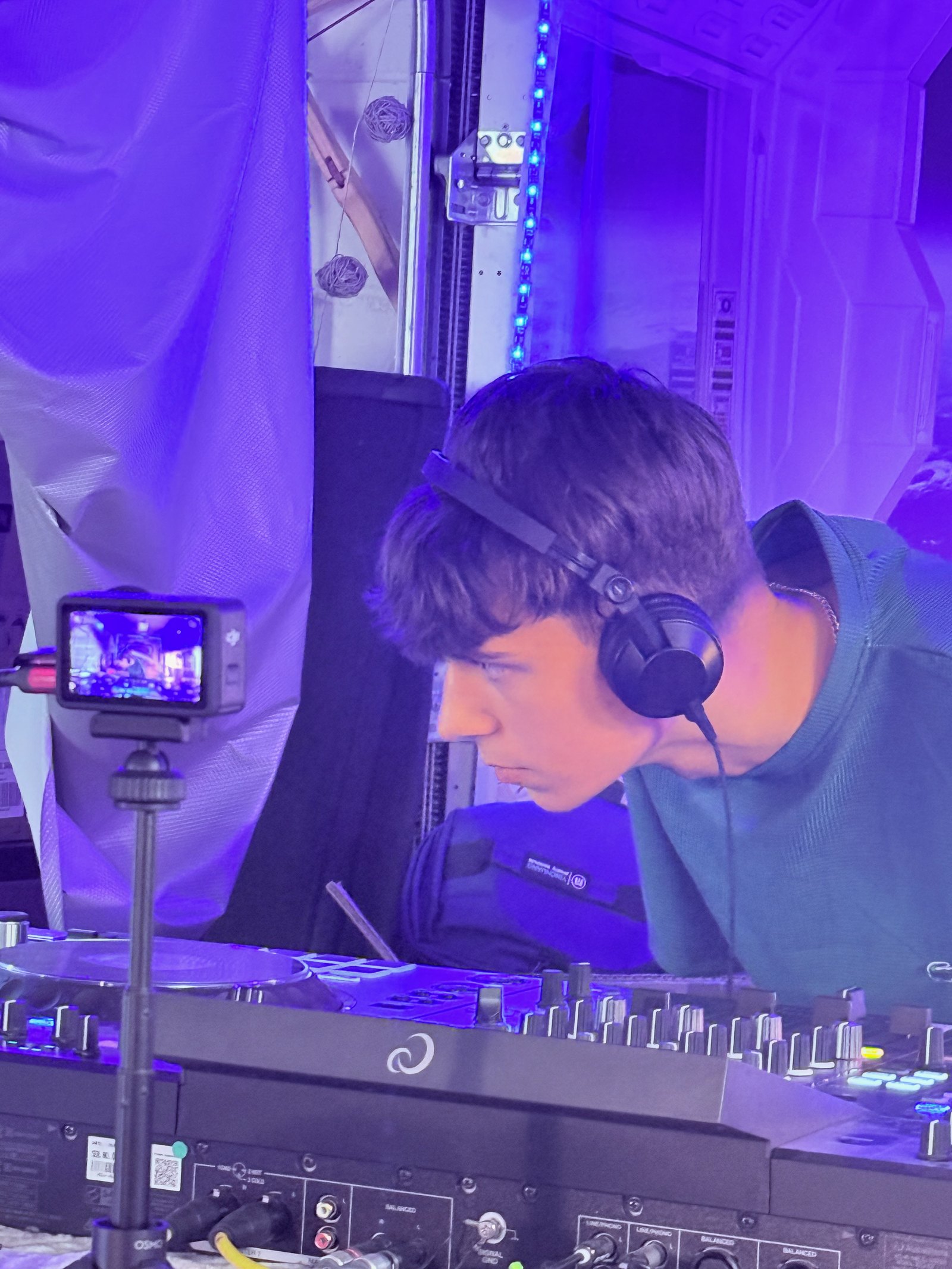 Chewbear in headphones, leaning in close over the mixer under purple light, listening.